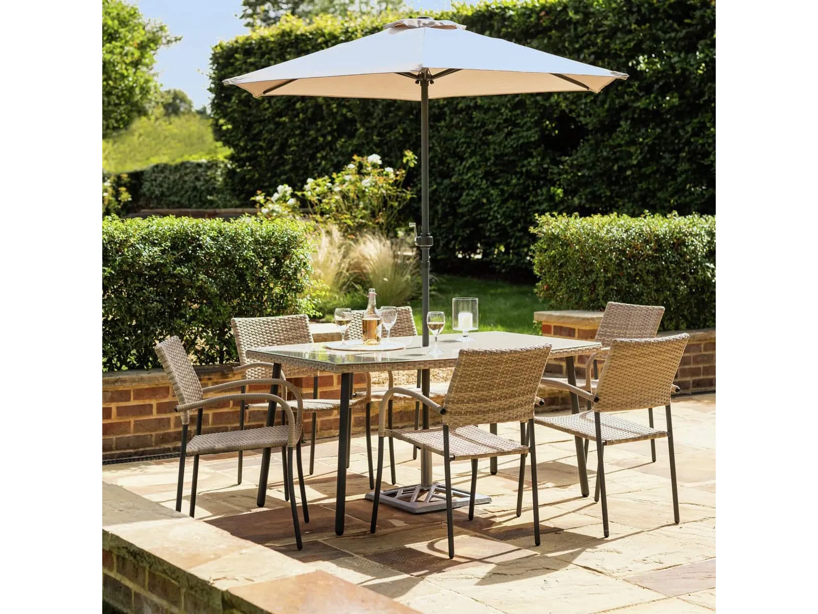 Outdoor dining table with glass top and rattan trim with 6 rattan dining chairs and a parasol