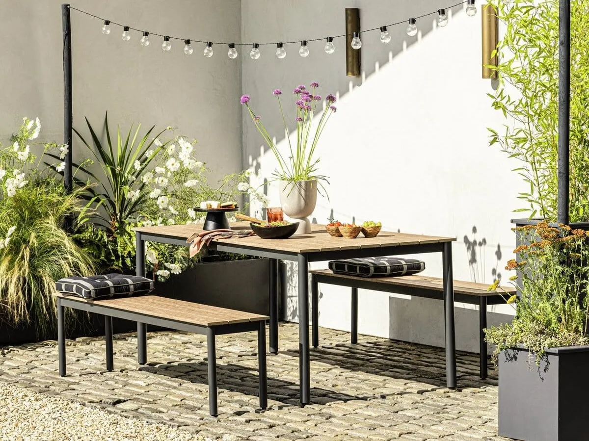 Outdoor dining table with wooden top and black metal frame with a pair of matching benches
