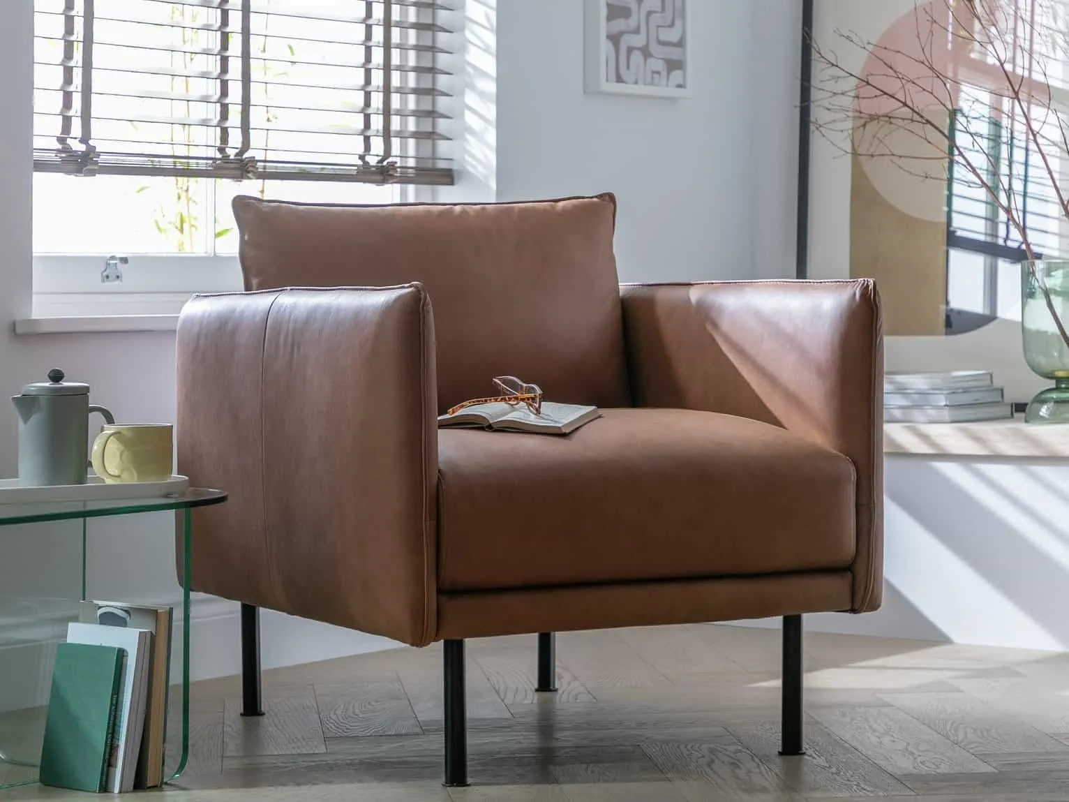 Tan leather armchair with slender armrests and black metal legs